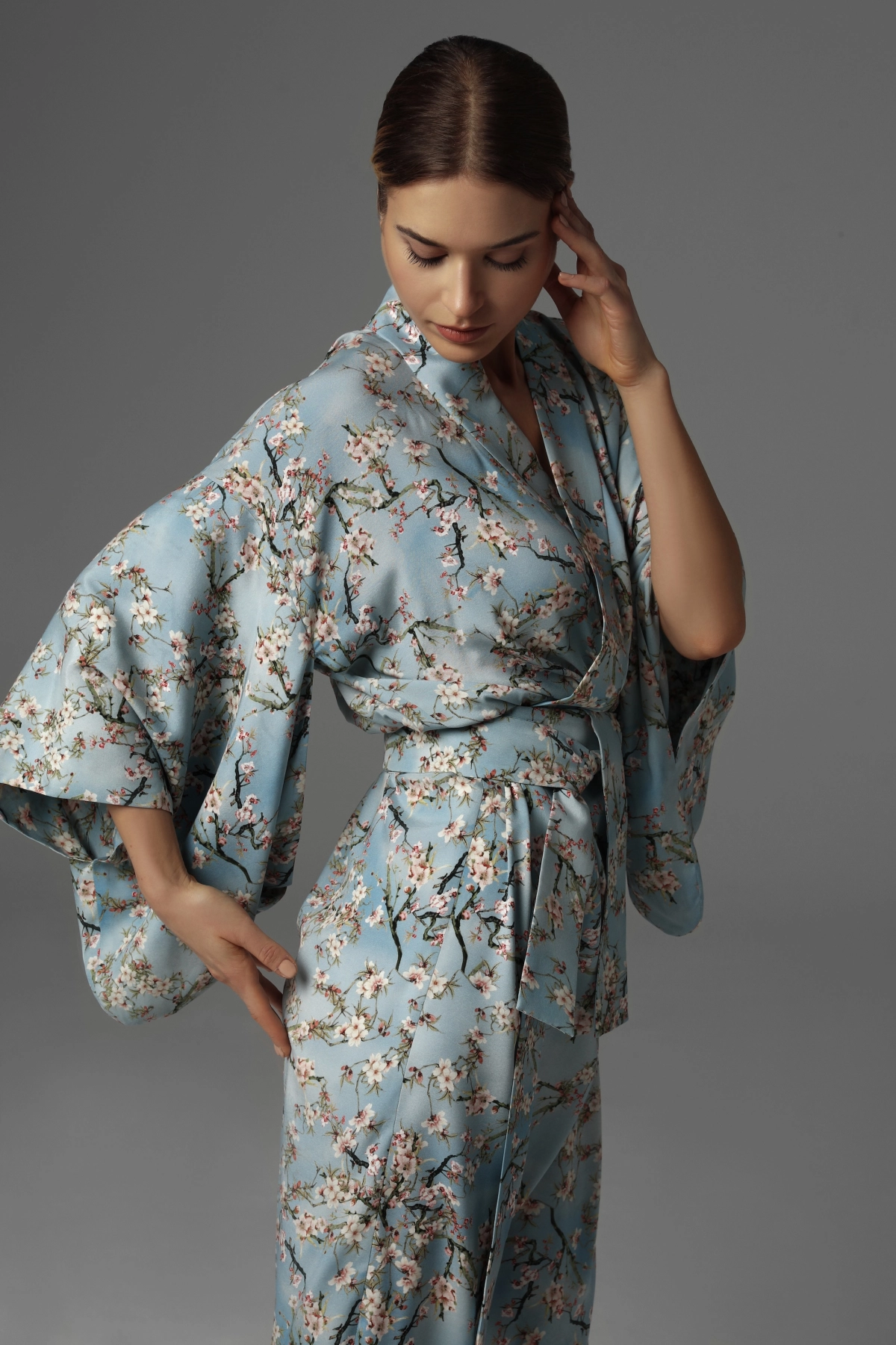 A model presenting the side of a kimono, showing the sleeves and cherry blossom pattern.