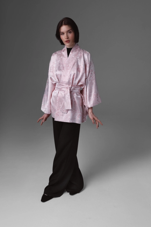 A model walking ahead presenting a short kimono in a delicate pink colour.
