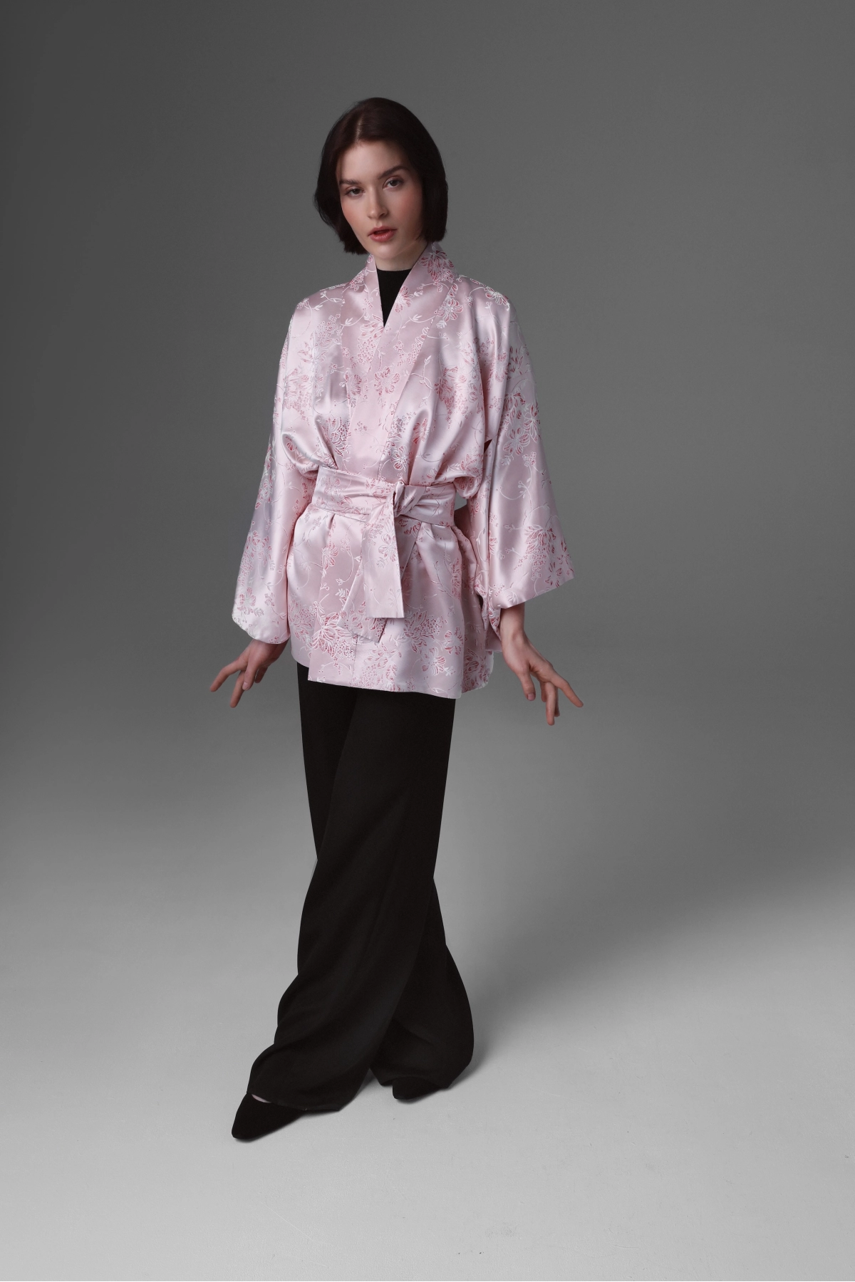 A model walking ahead presenting a short kimono in a delicate pink colour.