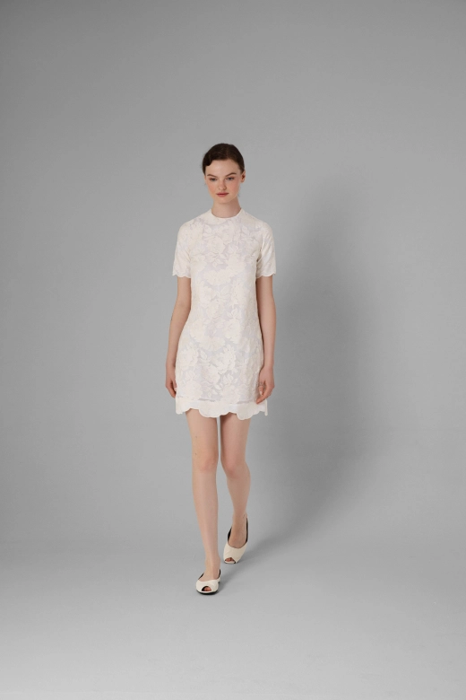 Close-up of embroidered pattern and scalloped hem of the ecru dress