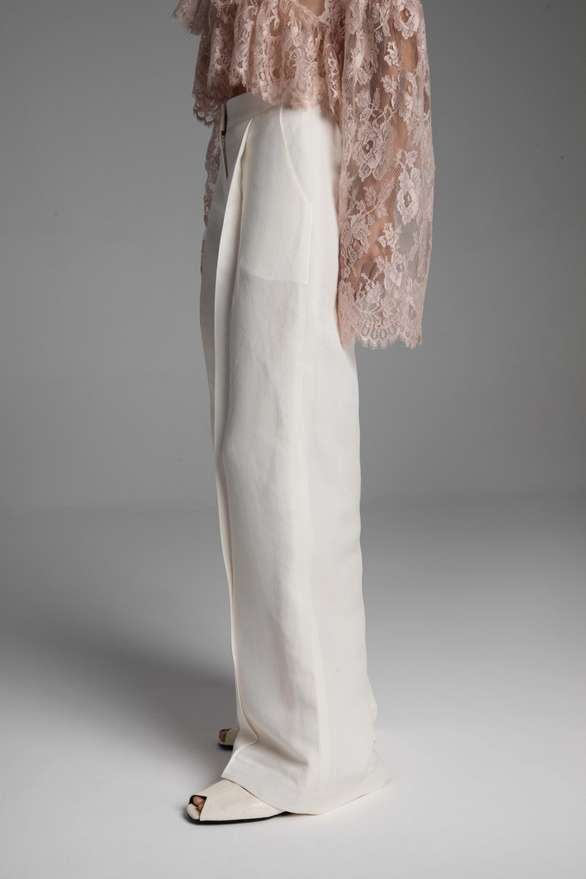 Close-up of the diagonal twill weave of the linen and silk fabric and precise pleats of Monika Adamska trousers.