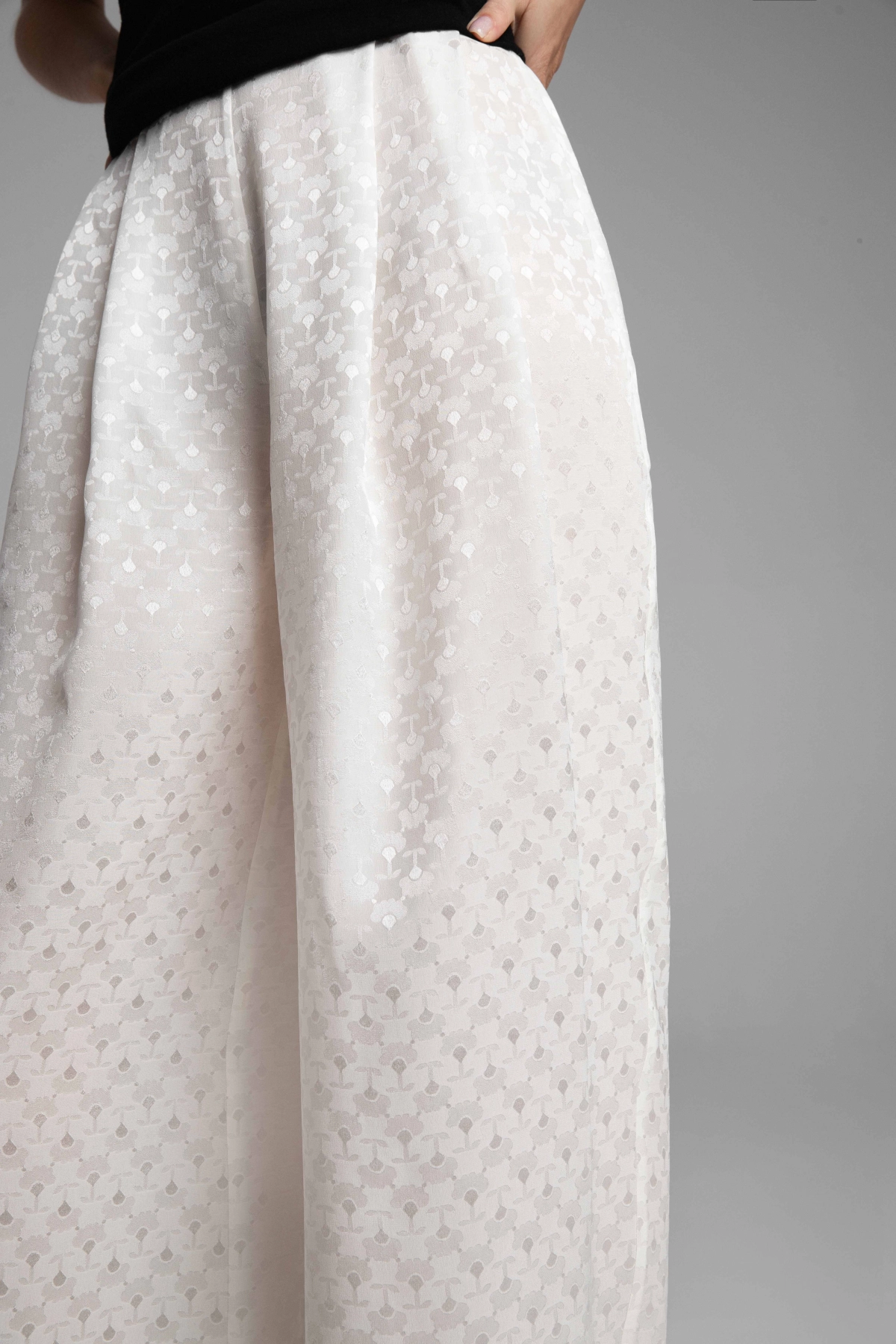 Detail of the deep pleats and the weave structure of the off-white silk jacquard trousers.
